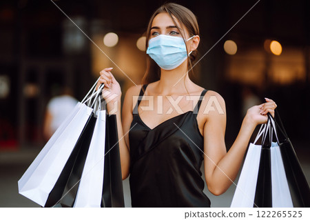 Fashionable woman in protective medical mask with shopping bags walking near mall. Covid-19. 122265525