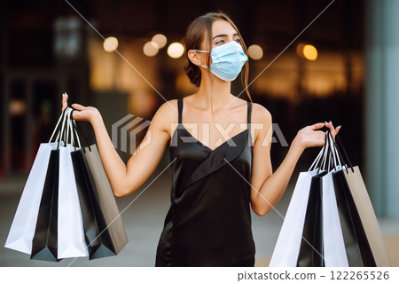 Fashionable woman in protective medical mask with shopping bags walking near mall. Covid-19. 122265526
