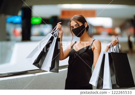Young woman in protective black medical mask on her face with shopping bags in the mall.Covid-2019. Young woman in protective black medical mask on her face with shopping bags in the mall.Covid-2019. 122265533