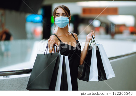 Fashionable woman in protective medical mask with shopping bags walking in the mall. Covid-19. 122265543