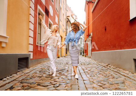 Happy women walk along city streets on sunny day. Young girlfriends having fun outdoors. Lifestyle. 122265781