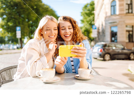 Two smiling woman are sitting in a cafe, drinking coffee. Fashion, beauty, blogging, tourism. Two smiling woman are sitting in a cafe, drinking coffee. Fashion, beauty, blogging, tourism. 122265798