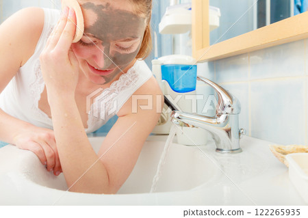 woman removing facial clay mud mask in bathroom 122265935