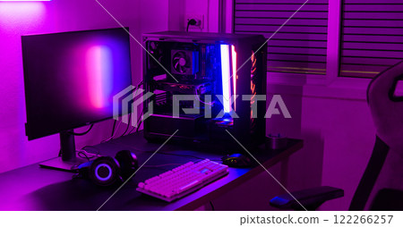 A computer setup with a purple light dark background, games transmission modern equipment, modern gaming PC on desk with keyboard mouse monitor, gamer work space concept A computer setup with a purple light dark background, games transmission modern equipment, modern gaming PC on desk with keyboard mouse monitor, gamer work space concept 122266257