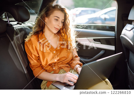 . Young freelancer woman working on a laptop in a car. Freelance, transportation concept. 122266810