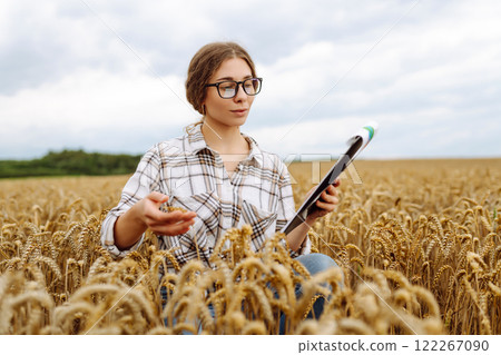 Young female farmer checking crop growth with clipboard in golden wheat field. Smart farming. 122267090