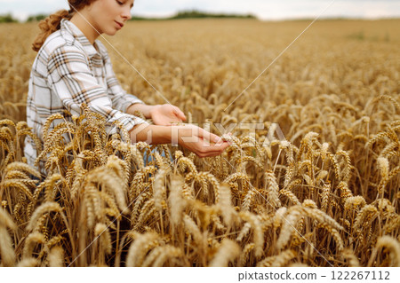 A woman agronomist studies the golden harvest of wheat on an agricultural field. Agriculture. 122267112