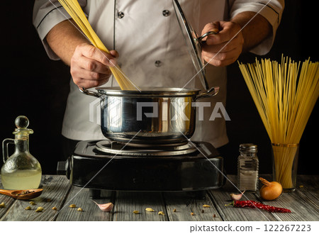 A skilled cook skillfully handles strands of spaghetti while preparing to boil them. The kitchen is adorned with fresh herbs and seasonings, creating an inviting atmosphere for culinary creativity A skilled cook skillfully handles strands of spaghetti while preparing to boil them. The kitchen is adorned with fresh herbs and seasonings, creating an inviting atmosphere for culinary creativity 122267223