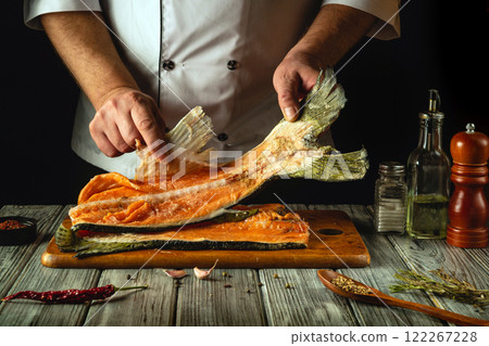 This dynamic kitchen moment captures a skilled chef filleting a fresh piece of fish on a wooden cutting board, surrounded by spices and herbs. The warm ambiance enhances the culinary artistry This dynamic kitchen moment captures a skilled chef filleting a fresh piece of fish on a wooden cutting board, surrounded by spices and herbs. The warm ambiance enhances the culinary artistry 122267228