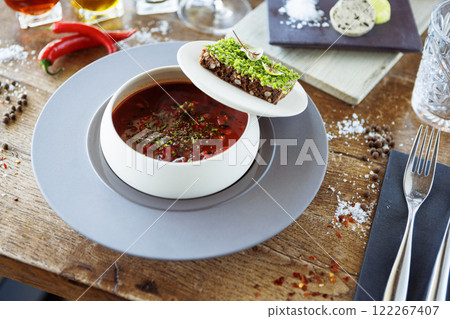 Borscht soup. Black Angus beef, beetroot, sour cream, toasted bread with smalec in a bowl. Delicious healthy food closeup served for lunch on a table in modern gourmet cuisine restaurant 122267407