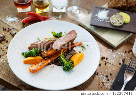 Duck fillet with sweet potato cream, roasted carrots, kale, beet-port sauce on white plate. Grilled and roasted poultry closeup served on a table for lunch in modern cuisine gourmet restaurant. Duck fillet with sweet potato cream, roasted carrots, kale, beet-port sauce on white plate. Grilled and roasted poultry closeup served on a table for lunch in modern cuisine gourmet restaurant. 122267411