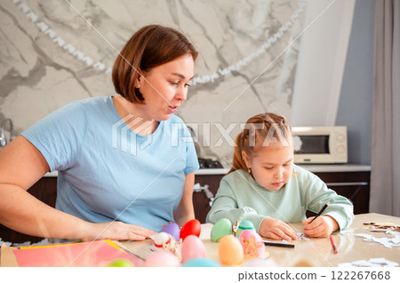 A little cute Caucasian girl and her mother are decorating paper rabbits for the Easter spring holiday. A family suites at a table and makes festive Easter decorations A little cute Caucasian girl and her mother are decorating paper rabbits for the Easter spring holiday. A family suites at a table and makes festive Easter decorations 122267668
