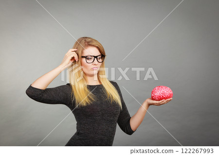 Woman in eyeglasses being confused holding brain Woman in eyeglasses being confused holding brain 122267993
