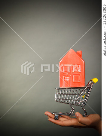 Woman hand holding shopping cart with house inside Woman hand holding shopping cart with house inside 122268009