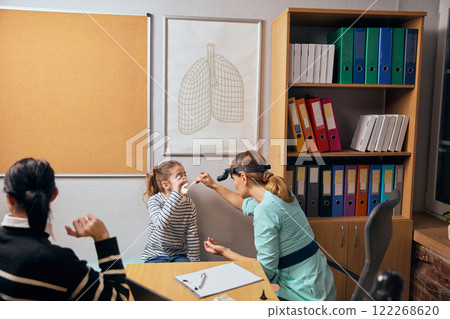 Female doctor with headlight performing nose and throat examination on young girl, highlighting ENT-focused healthcare. 122268620