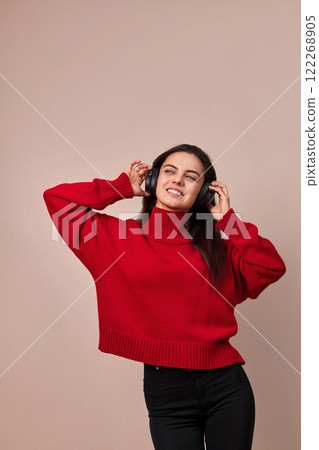 Happy woman wearing red sweater and headphones enjoying listening music on pink background. Happy woman wearing red sweater and headphones enjoying listening music on pink background. 122268905