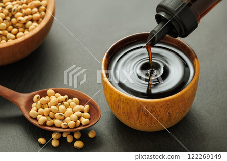 soy sauce pouring from bottle in bowl with splash and drop and dry soybeans on black stone background 122269149