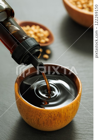 closeup soy sauce pouring from bottle in bowl with splash and drop and dry soybeans on black stone background closeup soy sauce pouring from bottle in bowl with splash and drop and dry soybeans on black stone background 122269150