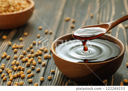 soy sauce pouring from spoon in bowl with splash and drop and dry soybeans on wooden table 122269153