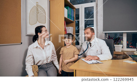 Bearded man, doctor listening to child lungs with stethoscope in medical office. Mother and child visiting pediatrician for health checkup 122269945