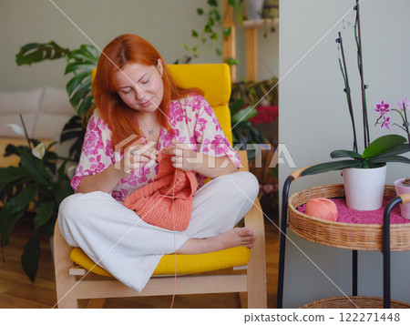 Young Woman knitting scarf in living room. doing crochet knits. 122271448