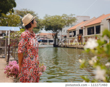 Young woman in ethnic dress and hat exploring the vibrant streets of Malacca, Malaysia. A blend of cultural heritage, colorful architecture, and tropical charm. Perfect travel and lifestyle moments. Young woman in ethnic dress and hat exploring the vibrant streets of Malacca, Malaysia. A blend of cultural heritage, colorful architecture, and tropical charm. Perfect travel and lifestyle moments. 122271460