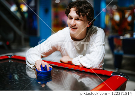 Young man enjoying an air hockey game in a vibrant arcade setting Young man enjoying an air hockey game in a vibrant arcade setting 122271814