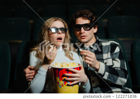 Young couple enjoying a suspenseful movie while eating popcorn Young couple enjoying a suspenseful movie while eating popcorn 122271836
