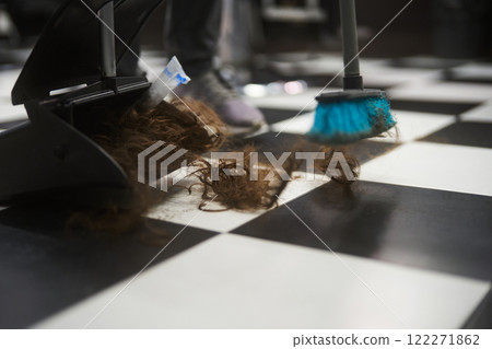 Cleaning hair on a checkered floor with a broom in a salon 122271862