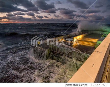 Dramatic Ocean Waves Crashing Onto a Seaside Boardwalk Under Active Skies 122271920