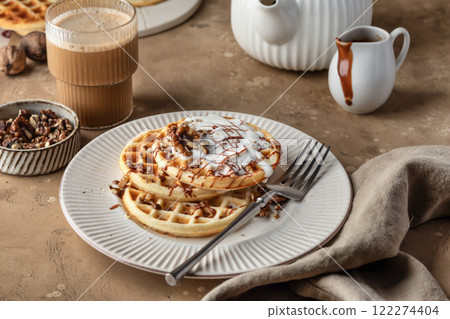 Belgian waffles with vanilla ice cream, nuts and chocolate topping served for breakfast on beige textured table background 122274404