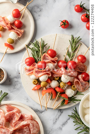 Skewers with mozzarella, ham, olives, peppers, tomatoes. Festive canapes or antipasti on white tray for party, top view Skewers with mozzarella, ham, olives, peppers, tomatoes. Festive canapes or antipasti on white tray for party, top view 122274408