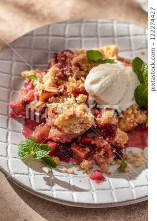 Apple crumble with ice cream on top decorated with mint leaves served in a plate on beige background in natural morning light close up Apple crumble with ice cream on top decorated with mint leaves served in a plate on beige background in natural morning light close up 122274427