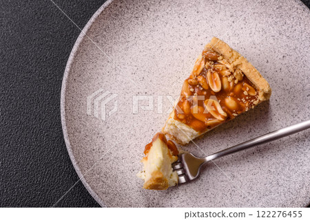 Delicious fresh cheesecake caramel peanut cake with cream and nuts on a ceramic plate on a dark concrete background Delicious fresh cheesecake caramel peanut cake with cream and nuts on a ceramic plate on a dark concrete background 122276455
