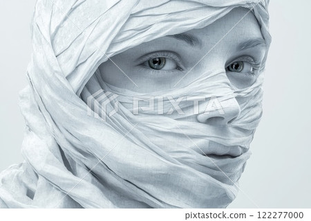 Mysterious figure wrapped in white fabric with captivating gaze in minimalist setting Mysterious figure wrapped in white fabric with captivating gaze in minimalist setting 122277000