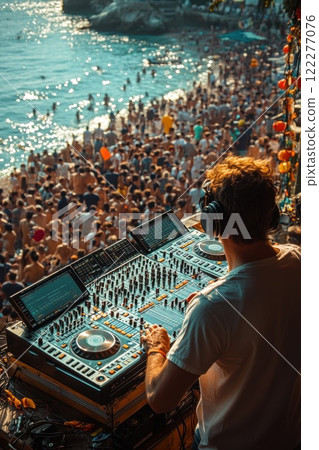 Crowd enjoying vibrant beach party as DJ performs in sunlit coastal setting, creating energetic atmosphere with pulsating music 122277076