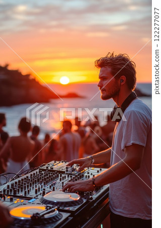 Sunset beach party with DJ performing live as guests enjoy the vibrant atmosphere with a stunning orange and purple sky over the ocean 122277077