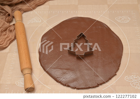 Christmas homemade baking, brown cocoa dough for baking gingerbread with tree shaped cutter, rolling pin on the table 122277102