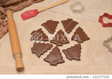 Christmas homemade baking, brown cocoa dough cut into tree shapes for baking gingerbread, cutter, rolling pin, spatula on the table 122277103