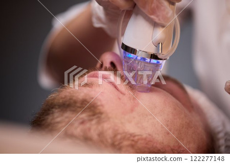 A man is currently undergoing a specialized facial treatment within a serene spa setting A man is currently undergoing a specialized facial treatment within a serene spa setting 122277148