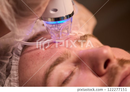 A man is currently undergoing a specialized facial treatment within a serene spa setting 122277151