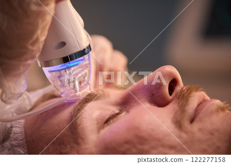 A man is currently undergoing a specialized facial treatment within a serene spa setting 122277158