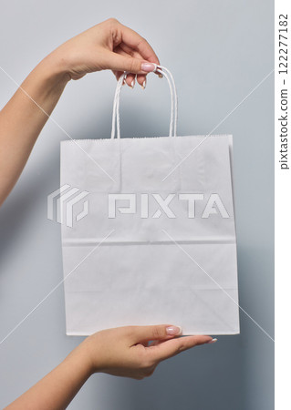 Hands Gently Holding a Clean and Pristine White Shopping Bag while Wearing Protective Gloves 122277182