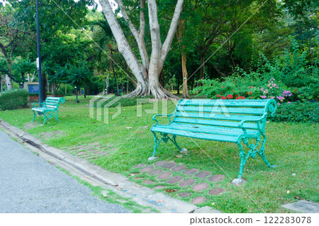 serene park scene featuring two vintage green benches surrounded by lush greenery and colorful flowers, inviting relaxation and tranquility 122283078