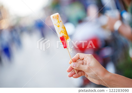 Delicious ice cream on stick held by hand in vibrant setting 122283090
