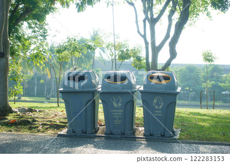 Trash bins in park with clear recycling instructions, surrounded by greenery and trees, promoting environmental awareness and cleanliness 122283153