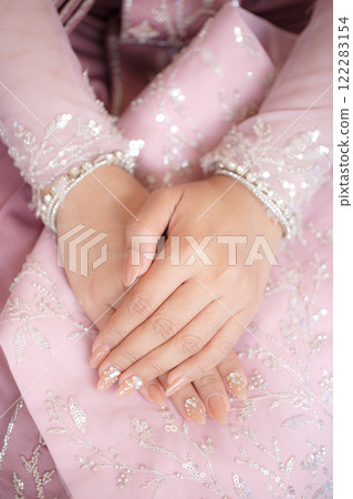 Elegant hands adorned with nail art resting on pink embroidered fabric 122283154