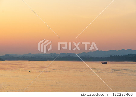 serene sunset over river, with soft orange and pink hues reflecting on water. Silhouettes of distant mountains create tranquil atmosphere 122283406