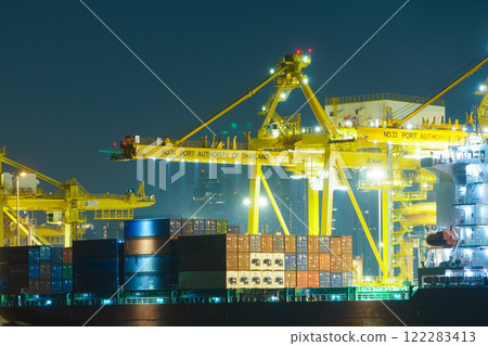 Night view of busy shipping port with cranes and containers in Thailand. vibrant lights create dynamic atmosphere, showcasing bustling activity of maritime trade Night view of busy shipping port with cranes and containers in Thailand. vibrant lights create dynamic atmosphere, showcasing bustling activity of maritime trade 122283413