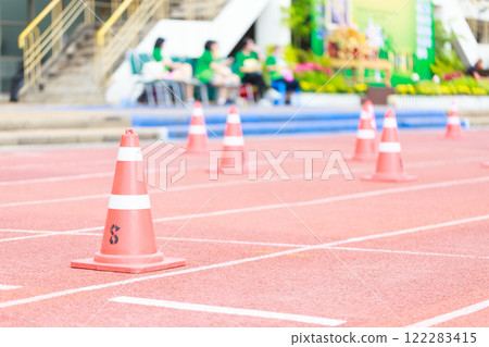 Orange traffic cones on red running track, marking lanes for sports event. vibrant colors create lively atmosphere, perfect for competitions and athletic activities 122283415